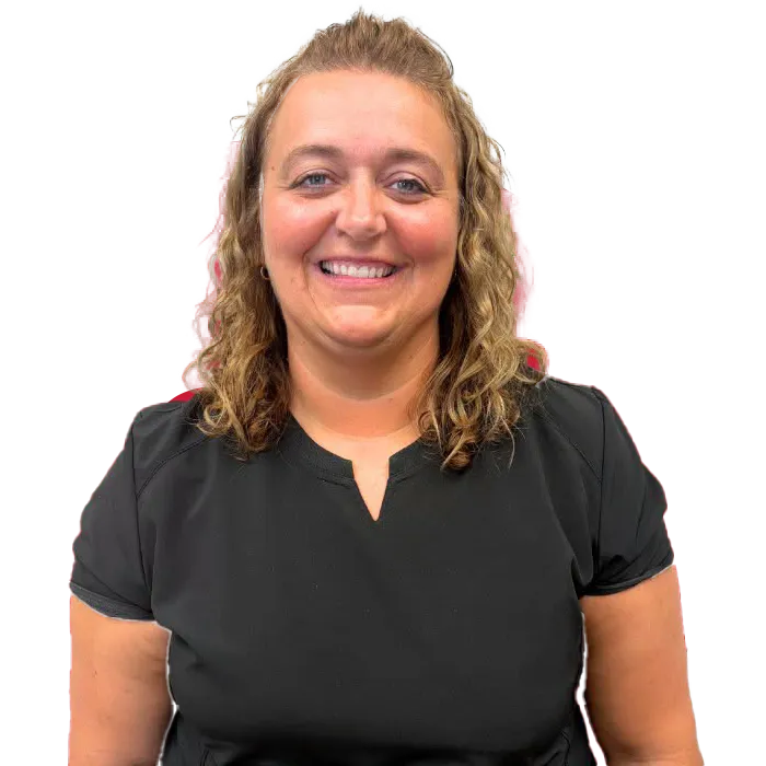 Smiling woman with curly blond hair wearing a black scrub top, standing against a light background.